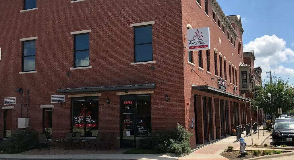 Red brick storefront with large windows and entrance doors on ground level, featuring signage and lounge seating visible inside
