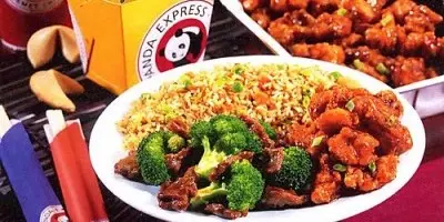 Plate of fried rice, broccoli, and crispy chicken with sauce, alongside beverages and additional dishes on table