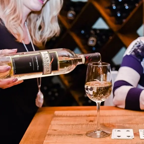 Person pouring white wine from a bottle into a glass at a wooden tasting counter
