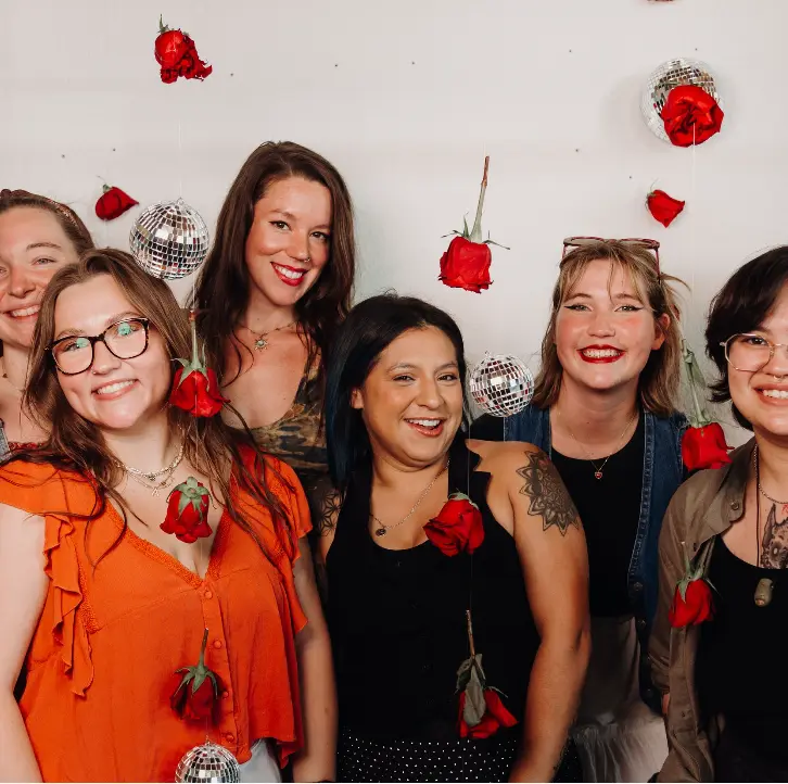 Group of six people smiling at camera with red roses and disco balls hanging in background