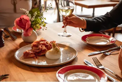 Formal dining table with plated appetizers, wine glasses, red-rimmed plates, and floral centerpiece, person in dark sleeve visible