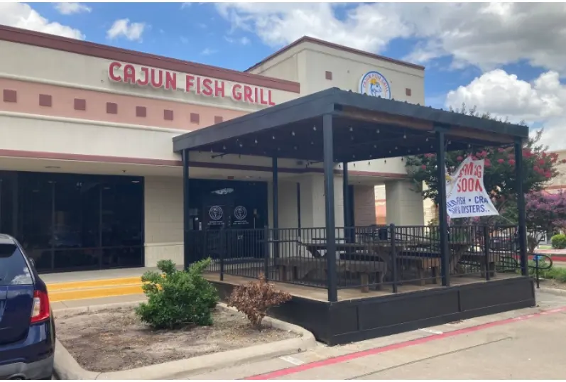 Restaurant exterior with covered entrance pavilion, signage visible on building facade, landscaping and parked vehicle