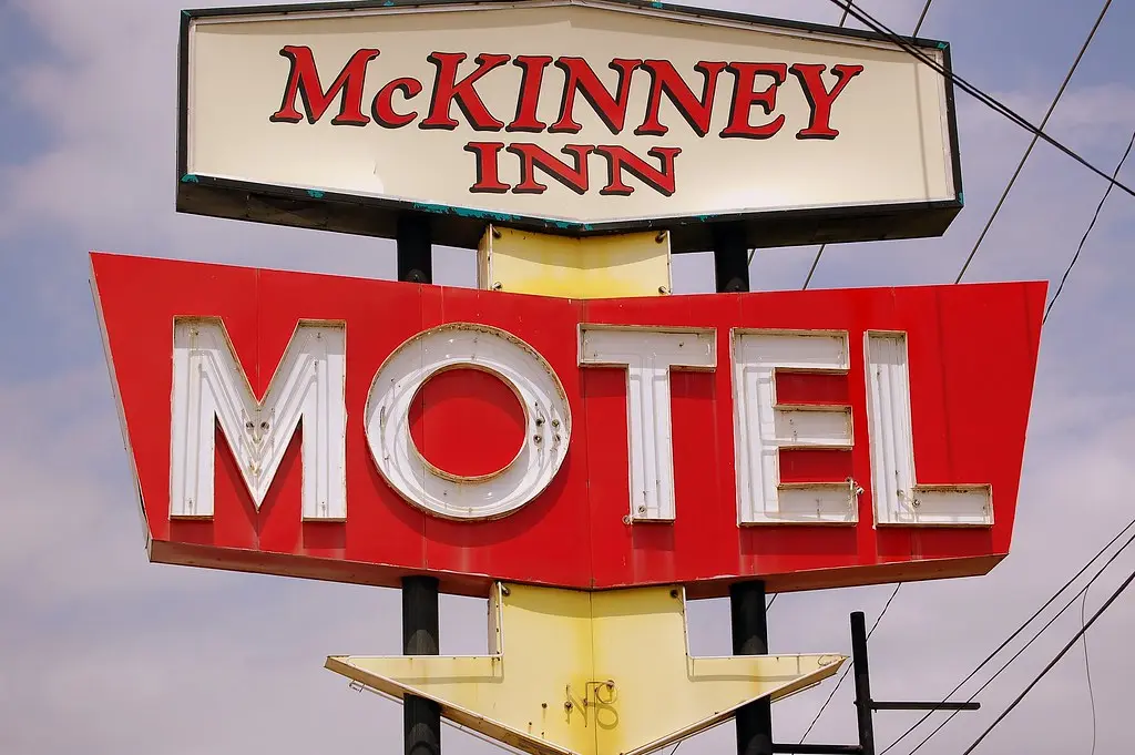 Vintage motel sign with red and white lettering against evening sky, yellow support post below