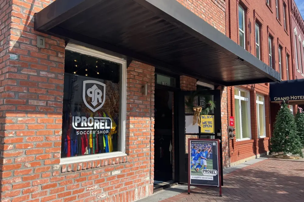 Storefront with black awning and dark entrance door, brick facade with shop window displaying logo and rainbow stripe design