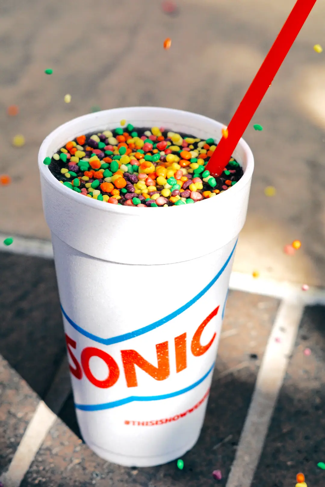 White cup filled with colorful candy balls and red straw, scattered candies on pavement