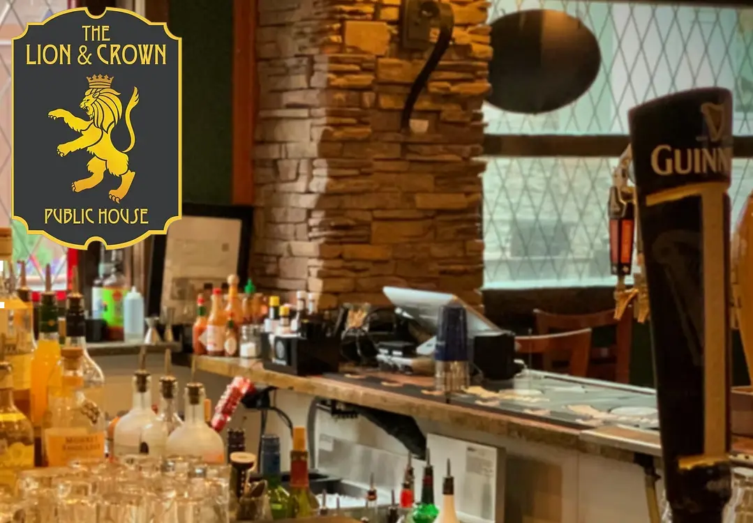 Bar counter with bottles, glasses, and beer taps inside a pub with brick walls and signage