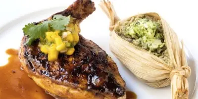 Seared duck breast with corn salsa and tamale wrapped in corn husk on white plate