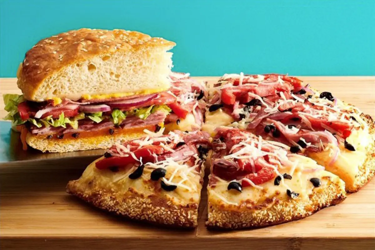 Toasted sandwich and sliced pizza with cured meats and toppings on wooden surface against turquoise background