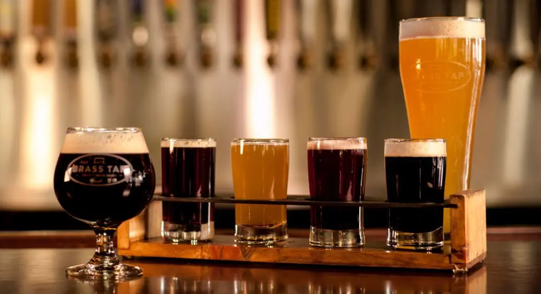 Flight of craft beers in various colors and styles arranged on a wooden paddle at a bar counter