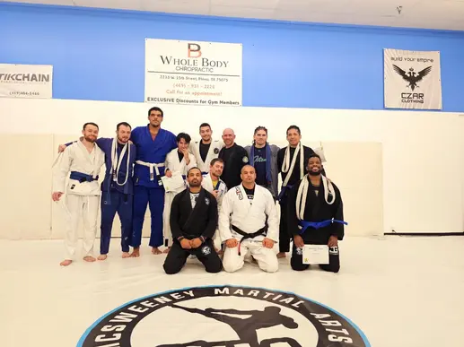 Group of martial arts students and instructors in gi uniforms standing on a mat in a training studio