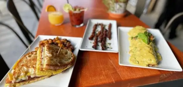 Brunch spread on a wooden table with a sandwich, smothered burrito, and crispy bacon