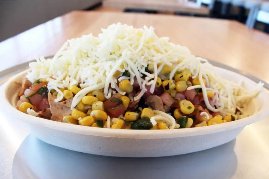 White bowl filled with corn, beans, meat, and topped with shredded cheese