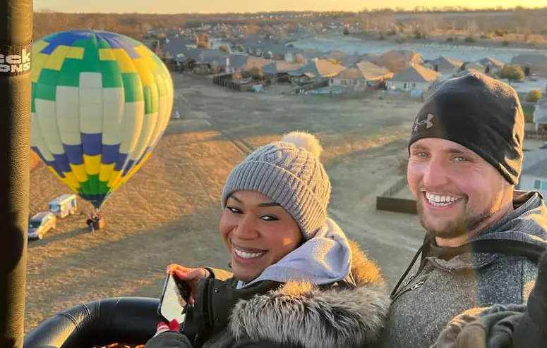 smiling couple in a hot balloon - ground in the background