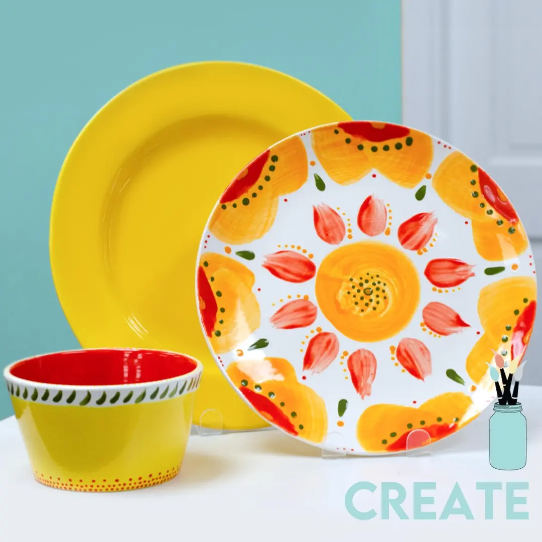 Colorful ceramic dinnerware set with yellow plate, patterned bowl with fruit design, and matching cup against turquoise background