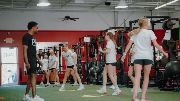 Small group of athletes exercising in a red and green fitness facility with equipment and machines visible in background