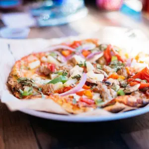 Flatbread pizza with melted cheese, fresh vegetables, and herbs on a white plate