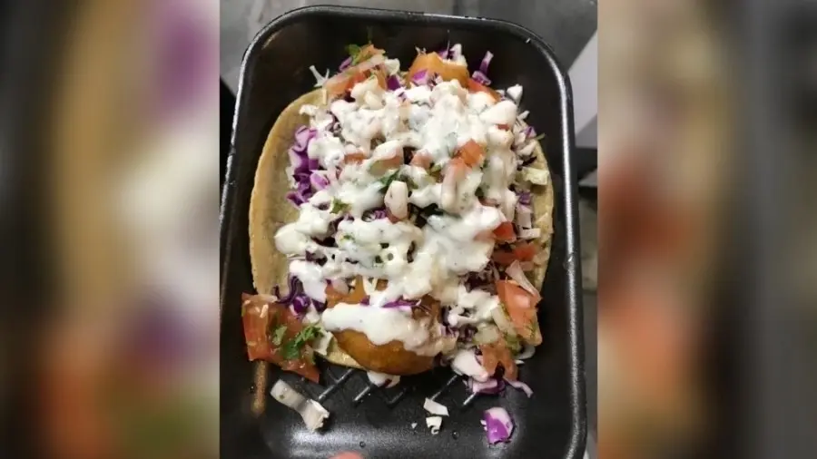 Crispy taco topped with shredded cheese, diced onions, and cilantro on a black plate