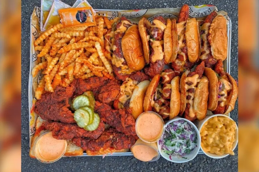 Overhead view of hot chicken tenders, loaded fries, hot dogs, and side condiments arranged on a dark surface