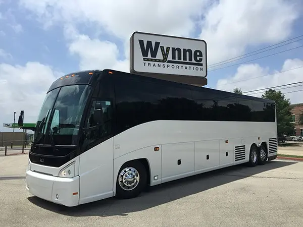 Large white and black charter bus parked in lot under company sign