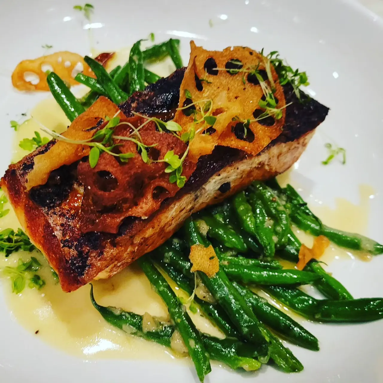 Seared salmon fillet with caramelized skin on bed of green beans, topped with crispy vegetables and microgreens