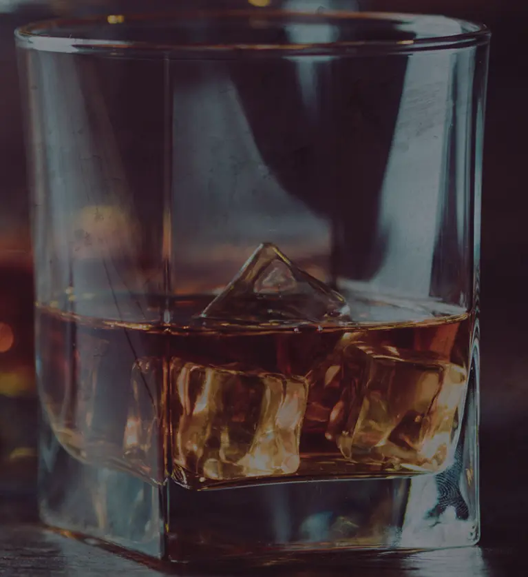 Glass filled with amber liquid and ice cubes against a blurred warm-toned background
