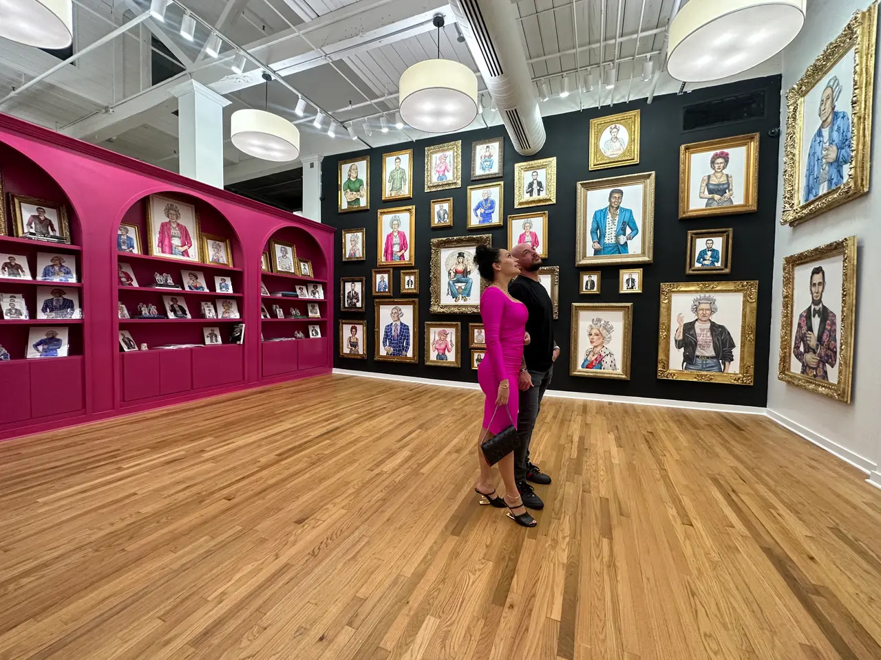 Woman standing in gallery with magenta shelving on left wall and black wall with framed portrait paintings on right