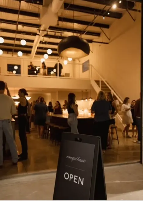 Interior of modern studio space with high ceilings, people mingling at an event, exposed wooden beams, and pendant lighting