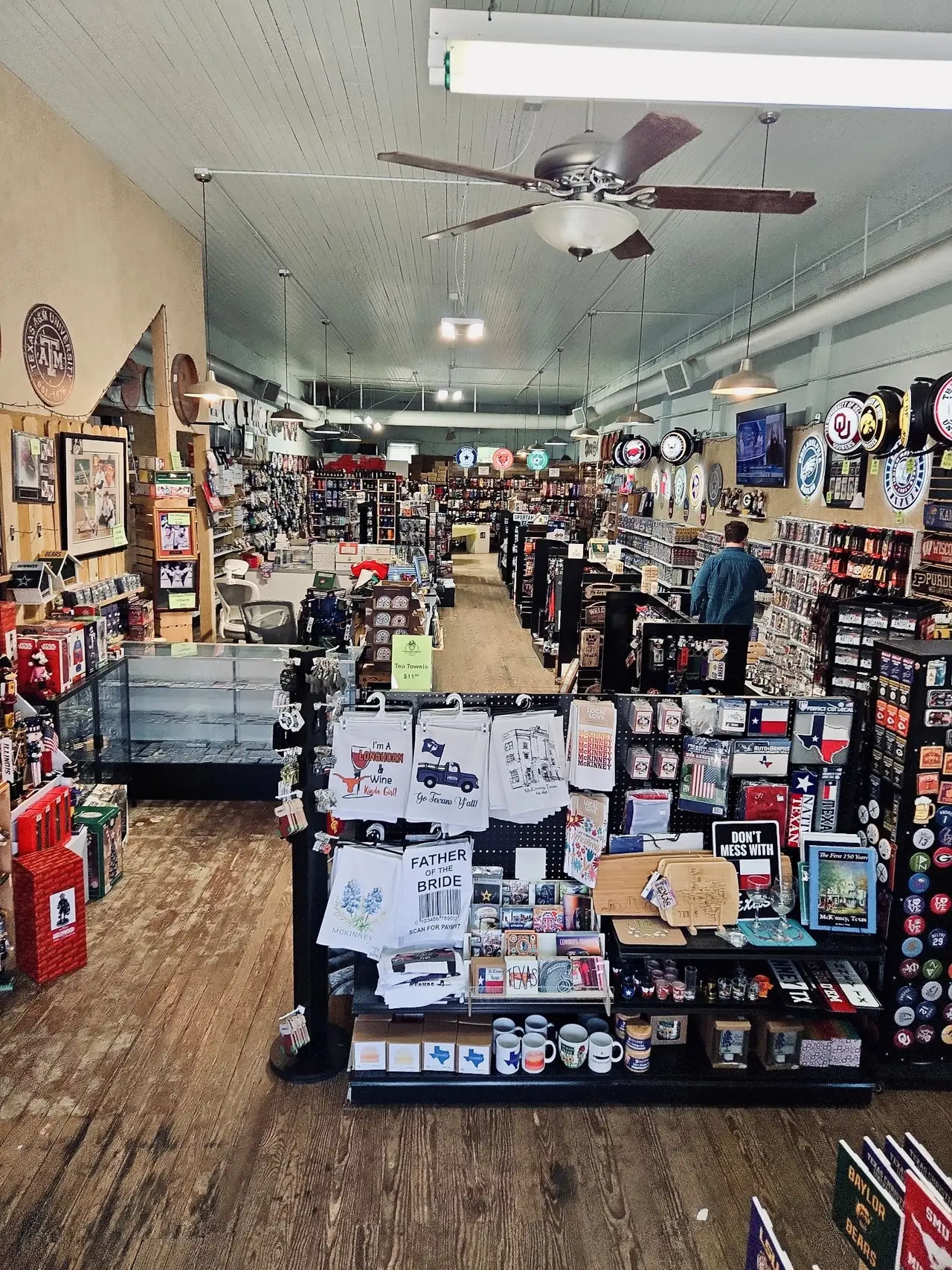 Interior of gift and sports memorabilia store with merchandise displays along walls, central display table, and wooden flooring throughout