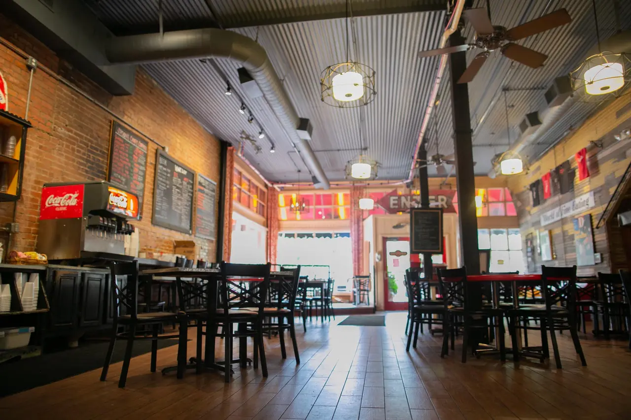 Interior of casual cafe with black chairs and tables, exposed brick walls, neon signs, and industrial ceiling in converted historic building