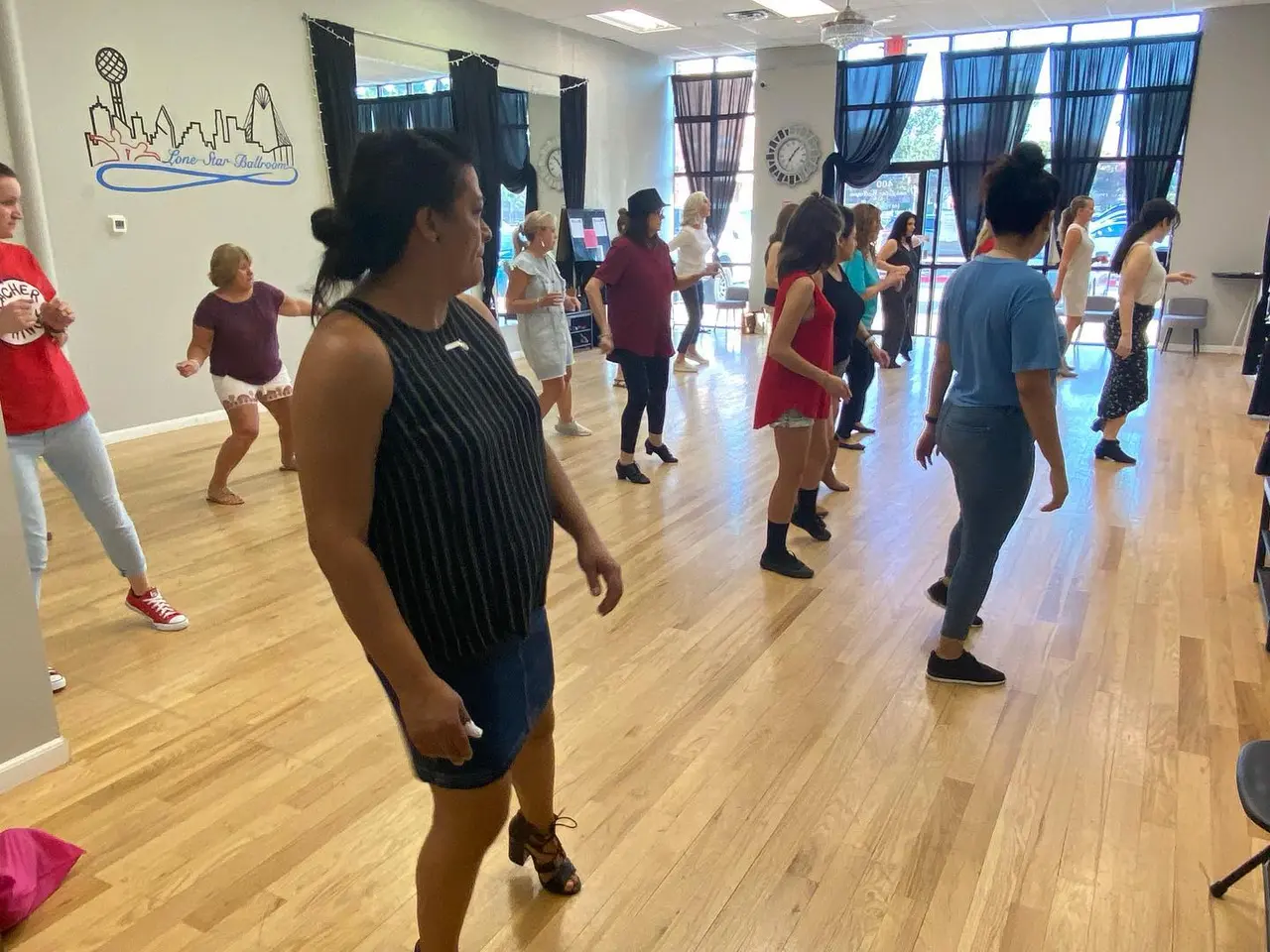 Group of children and adults dancing together in a bright studio with wooden floors and large windows