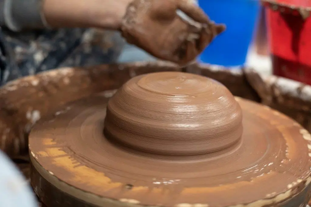 Potter's hands shaping clay on a spinning pottery wheel, creating a rounded vessel form