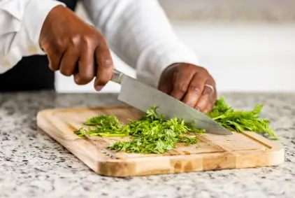 Chef chopping fresh green herbs on a wooden cutting board with a chef's knife