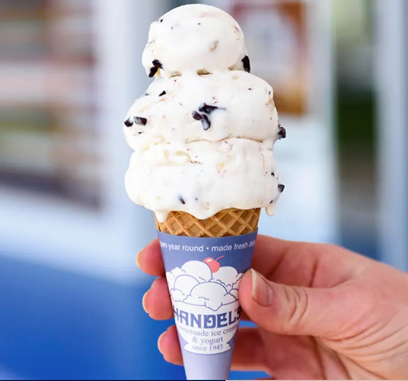 Hand holding a waffle cone with three scoops of vanilla ice cream studded with dark chocolate pieces