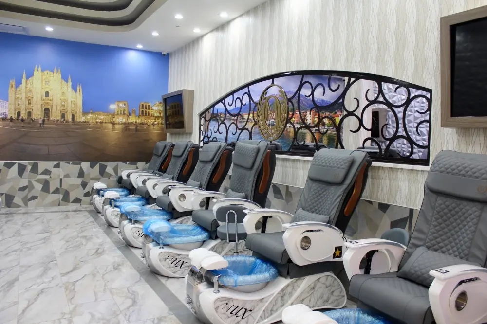 Row of pedicure stations with blue water basins and gray reclined chairs facing a mural of an ornate cathedral