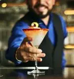 Bartender holding a cocktail with orange garnish and blue lighting in background