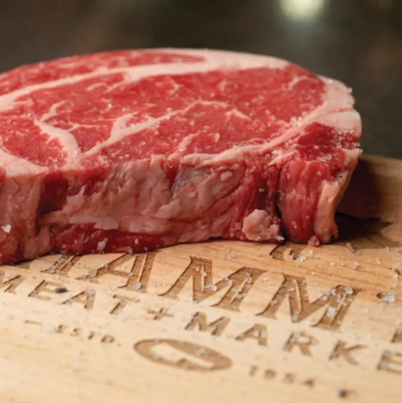 Raw ribeye steak on wooden cutting board with engraved text