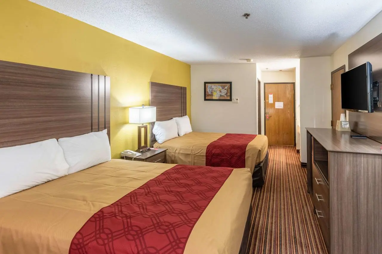 Hotel room with two double beds, yellow walls, wood headboards, red bed runners, flat-screen TV, and striped carpet