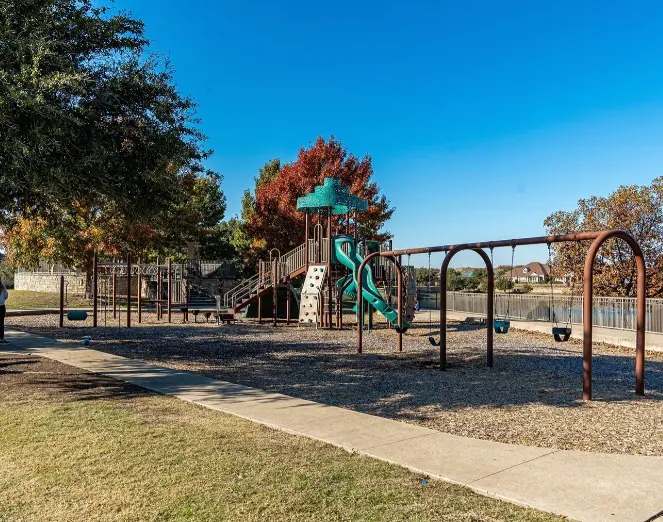 Playground with slide tower, climbing structures, and swings surrounded by trees and grass under clear blue sky