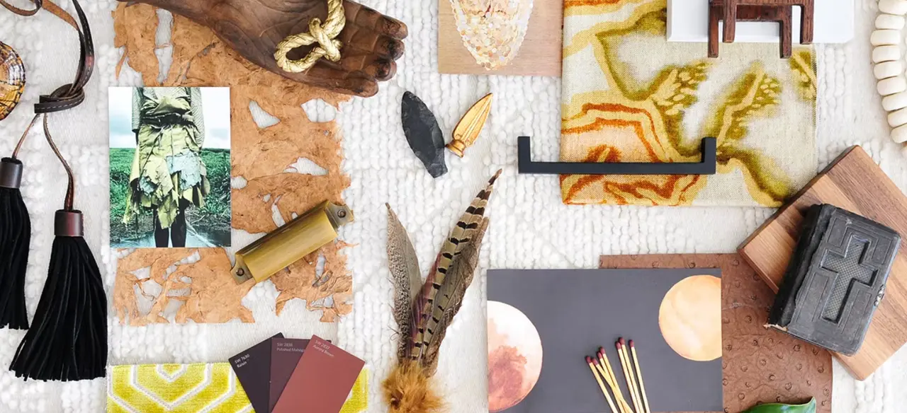 Flat lay arrangement of vintage and handmade objects including feathers, tassels, fabric swatches, natural materials, and decorative items on neutral surfaces