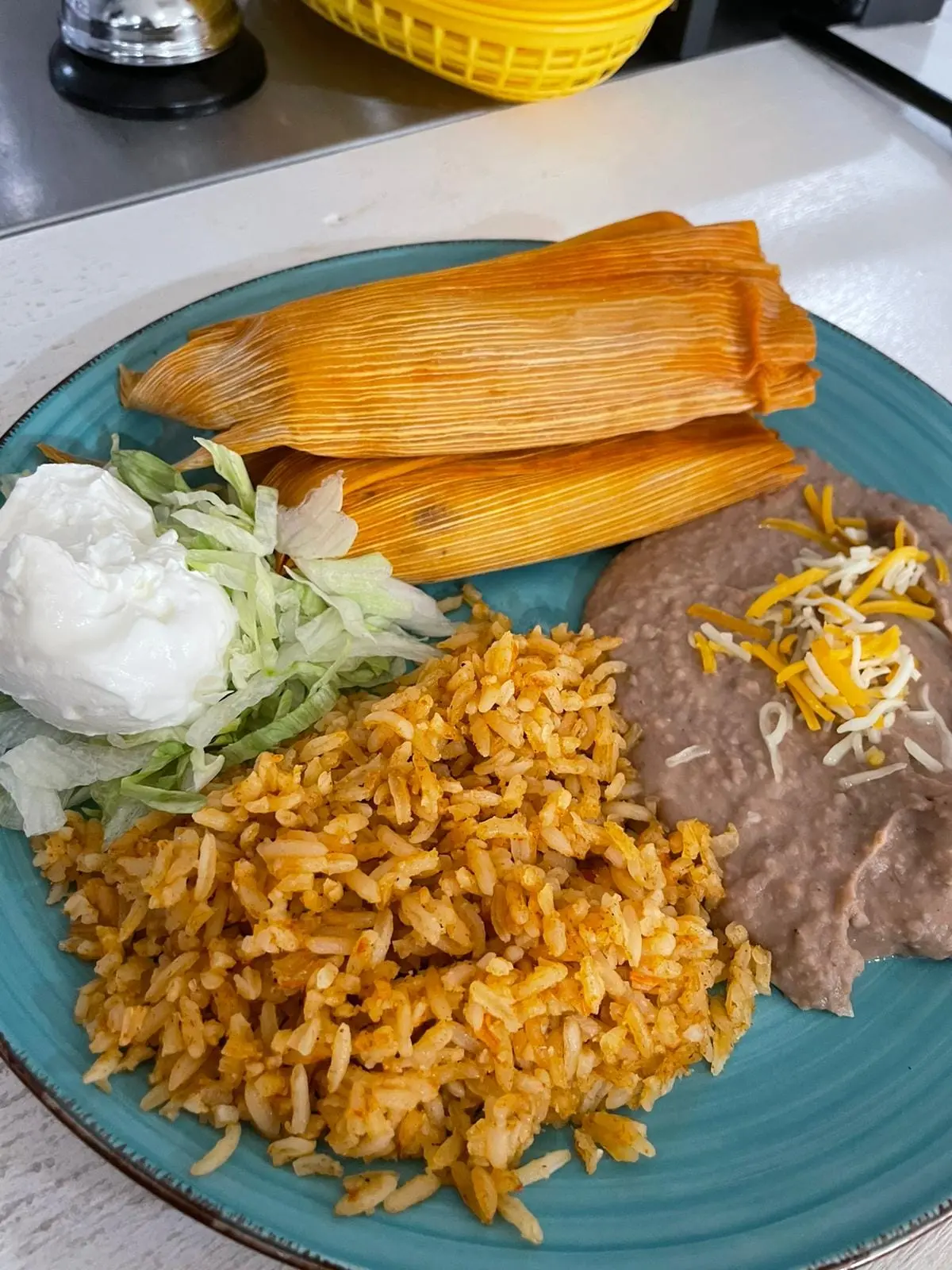 Plate with two tamales, red rice, refried beans, and shredded cabbage with sour cream