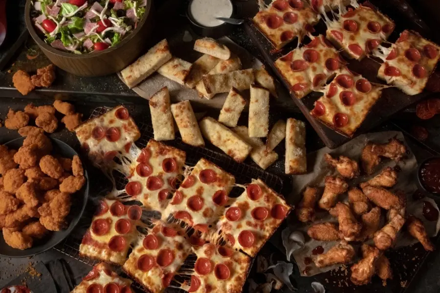 Overhead view of pizza slices, breadsticks, wings, and salad arranged on dark surfaces