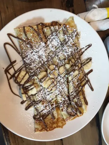 Crepe dusted with powdered sugar, drizzled with chocolate sauce, filled with sliced bananas on a white plate