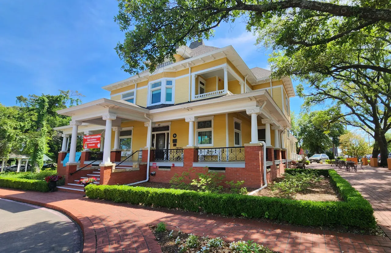 Big yellow house with hedge around red brick sidewalk leading to steps