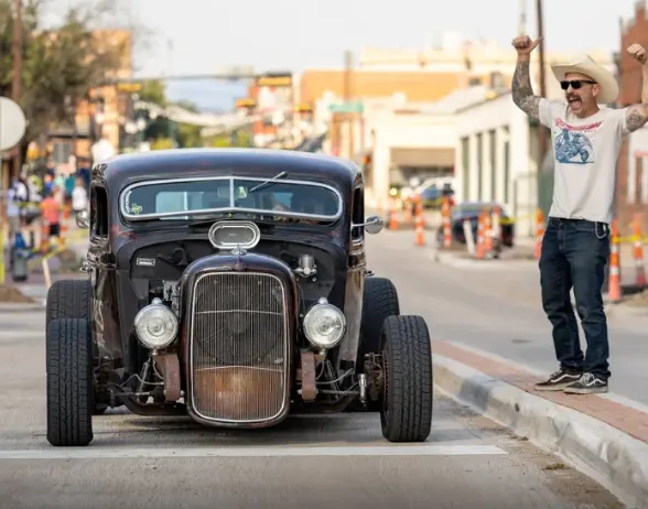 Black vintage hot rod with chrome details parked on street during daytime car show event