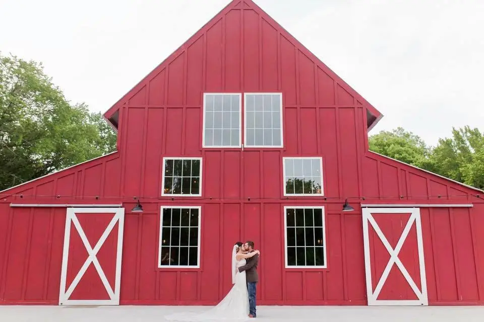 Couple standing in front of a red barn with white X-pattern doors and multiple windows