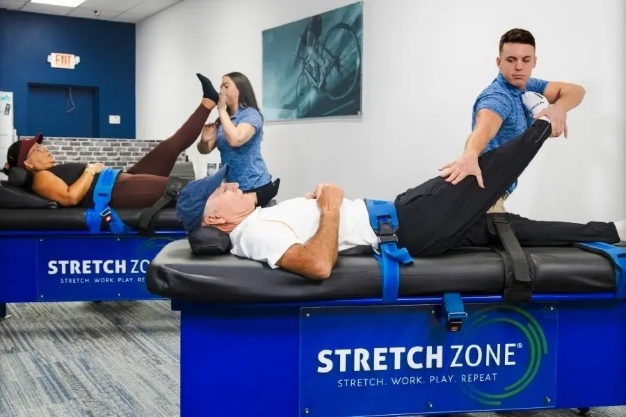 Certified practitioners assisting clients with assisted stretching on blue stretch tables in a studio