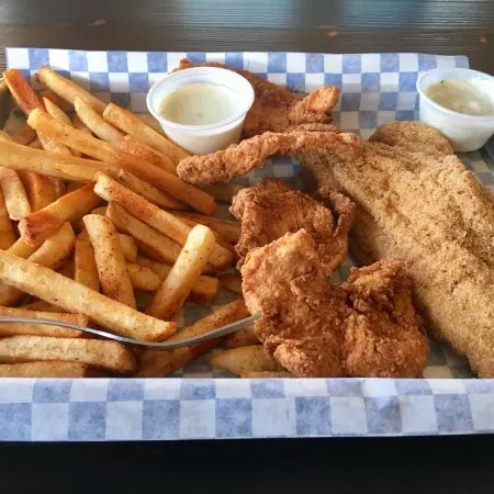 Fried chicken pieces and breaded fish fillet with French fries and white dipping sauces on checkered paper