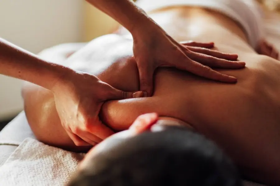 Massage therapist's hands applying pressure to client's shoulder and upper back on white linens