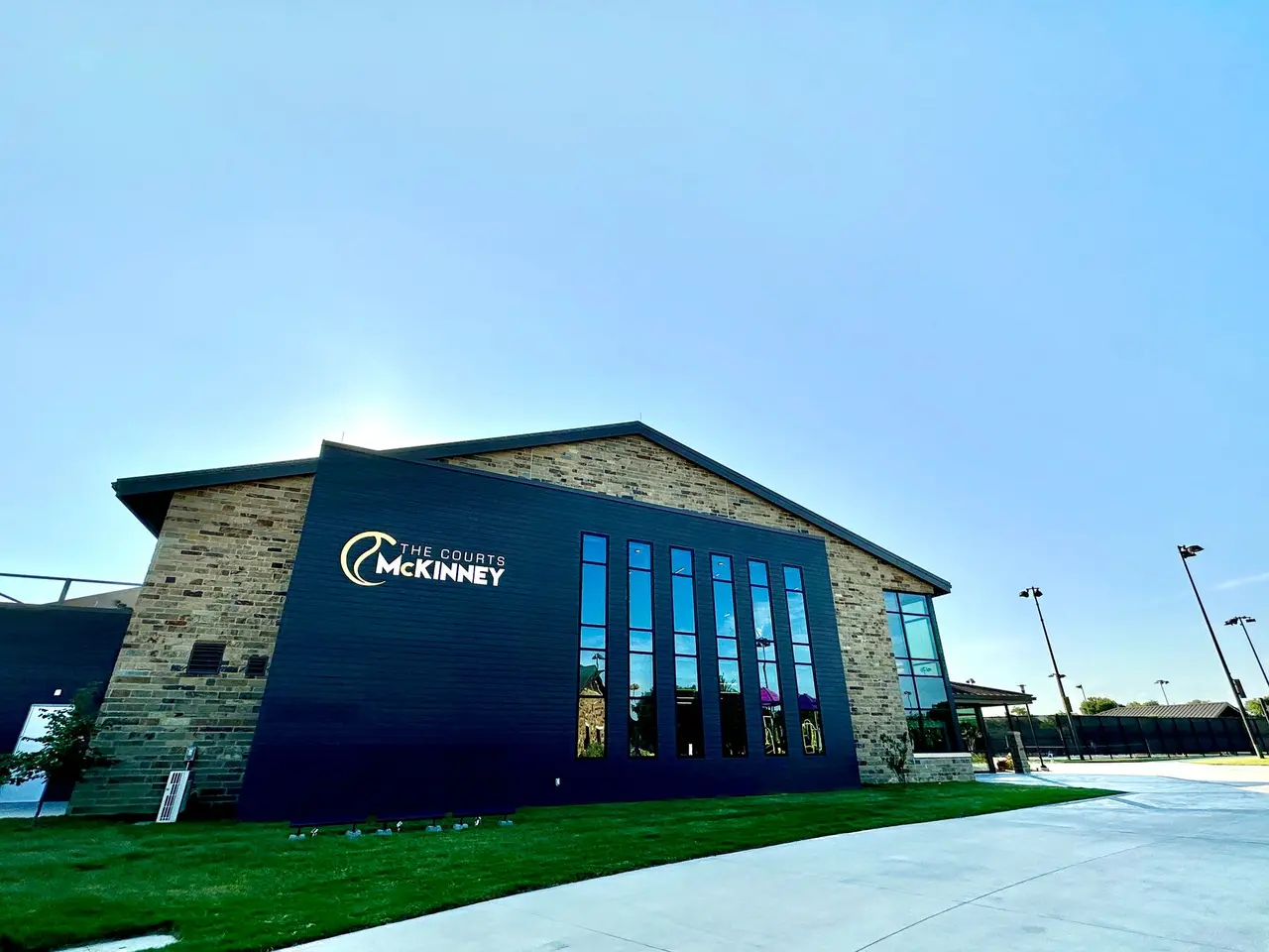 Modern tennis facility with blue-tinted exterior, stone accents, and large windows under clear sky