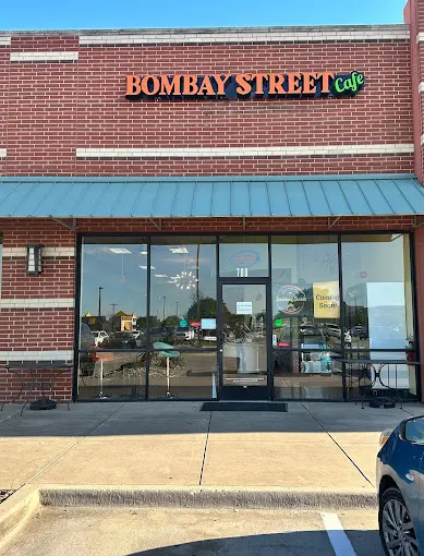 Brick storefront with large yellow signage reading "Bombay Street Cafe" and glass entry doors with interior seating visible
